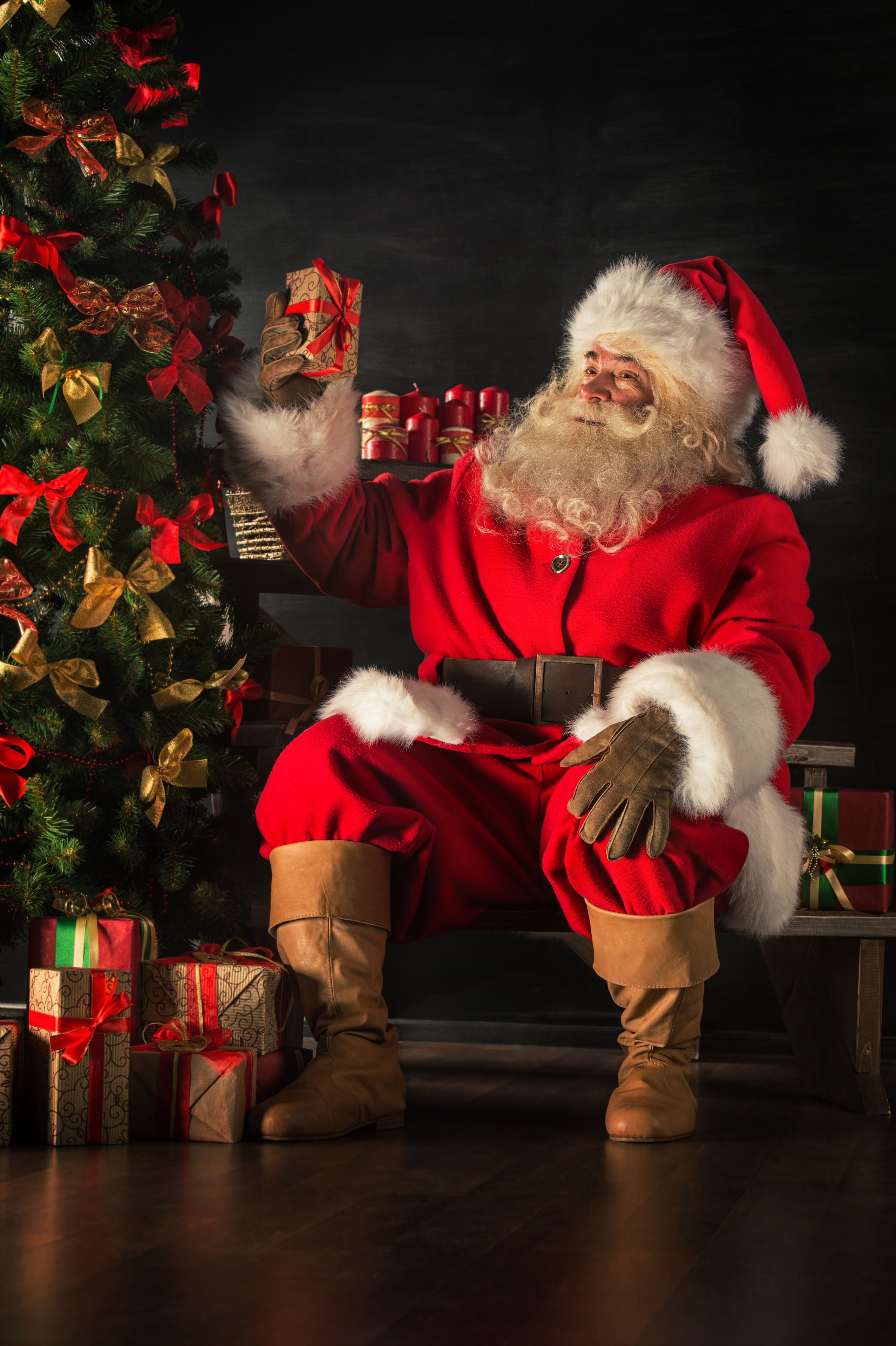 santa holding a gift next to a christmas tree